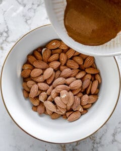 process showing spices being added to almonds in white bowl