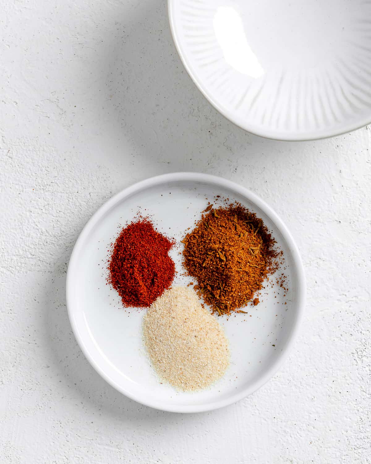 measured out spices in a white dish against a white background