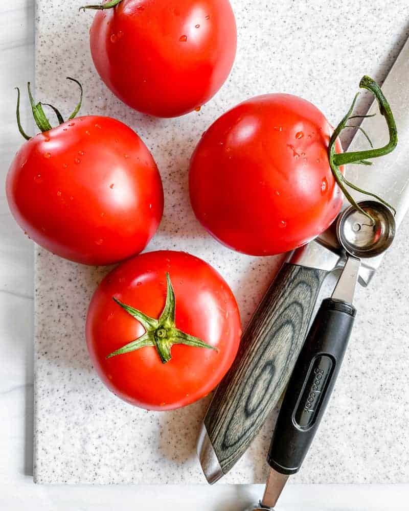 four raw tomatoes on a cutting board
