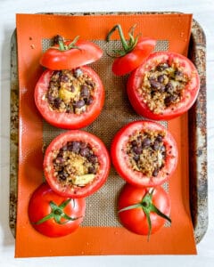 Stuffed tomatoes on a silpat-lined baking sheet.