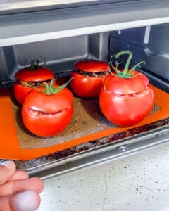 Stuffed tomatoes on a baking sheet being slid into an oven.