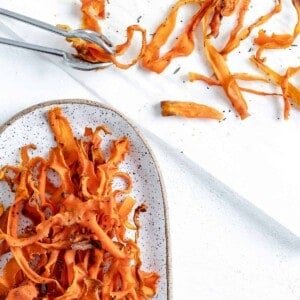 completed carrot fries in a white platter against a white background with carrot fries scattered in the background