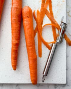 process of peeling carrots on white cutting board