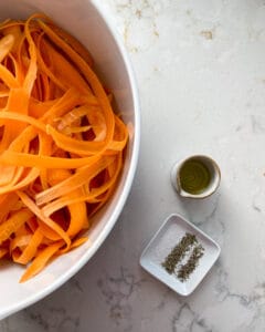 sliced carrot fries prior to being baked in a bowl with measured out ingredients against a white background
