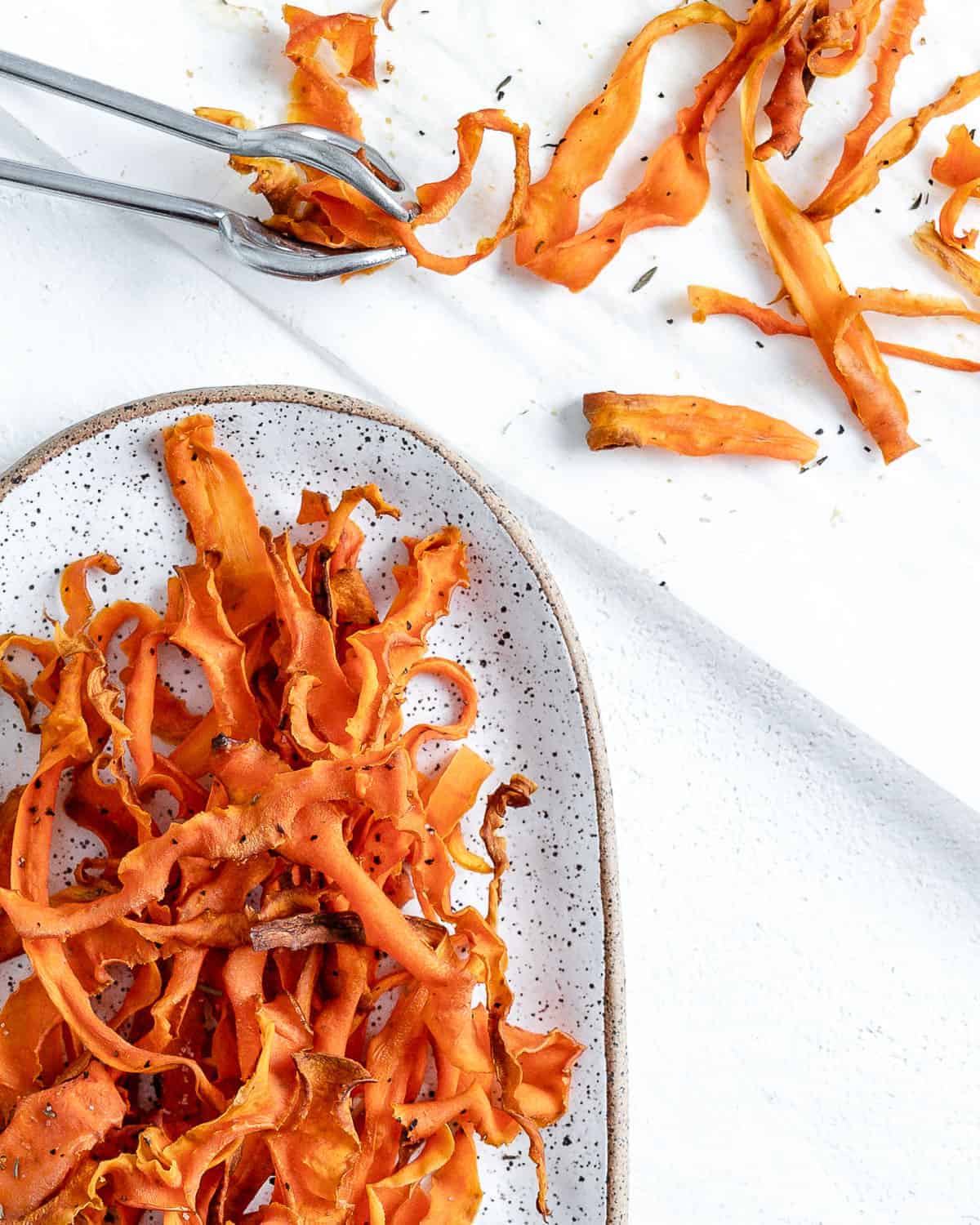completed carrot fries in a white platter against a white background with carrot fries scattered in the background