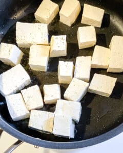process of adding cubed tofu to black pan