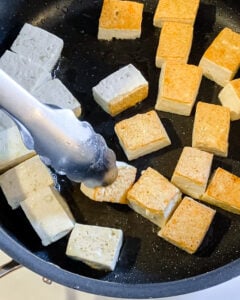 process of adding sauce to cubed tofu to black pan