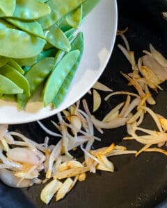 process of snow peas being adding to veggies on pan