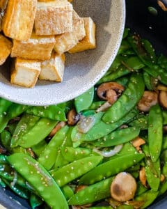 process of adding tofu to snow peas and veggies pan