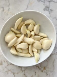 raw cloves of garlic in a white bowl against a white marble surface