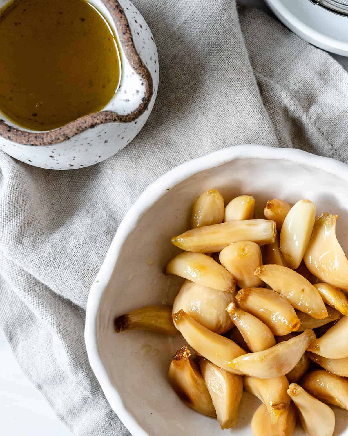 completed Stovetop Roasted Garlic in a white bowl against a white background with oil in the background