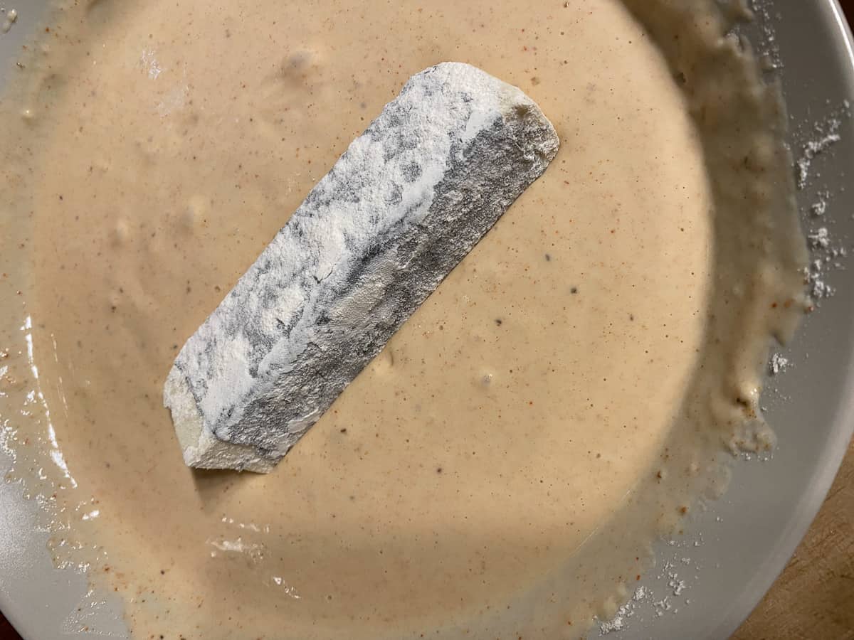 process shot of dipping and coating tofu strip into flour and milk mixture