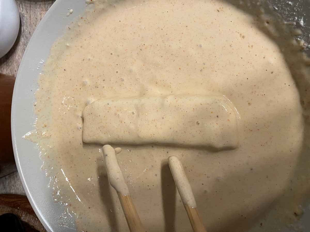 process shot of dipping and coating tofu strip into flour and milk mixture