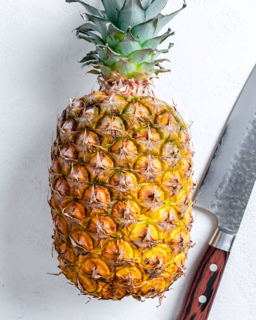 whole pineapple and cutting knife against white background