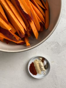 bowl of cut sweet potato fries in a bowl alongside a small bowl of spices