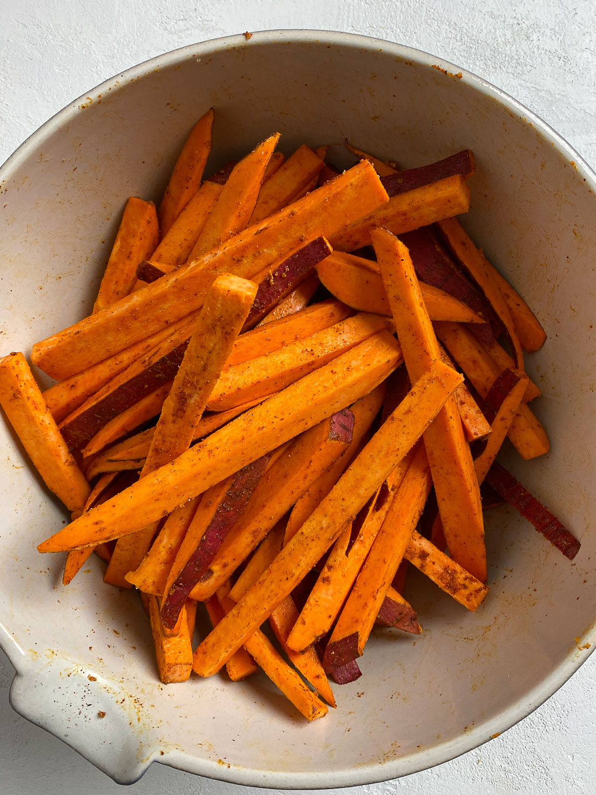 sliced sweet potato with seasonings in a bowl