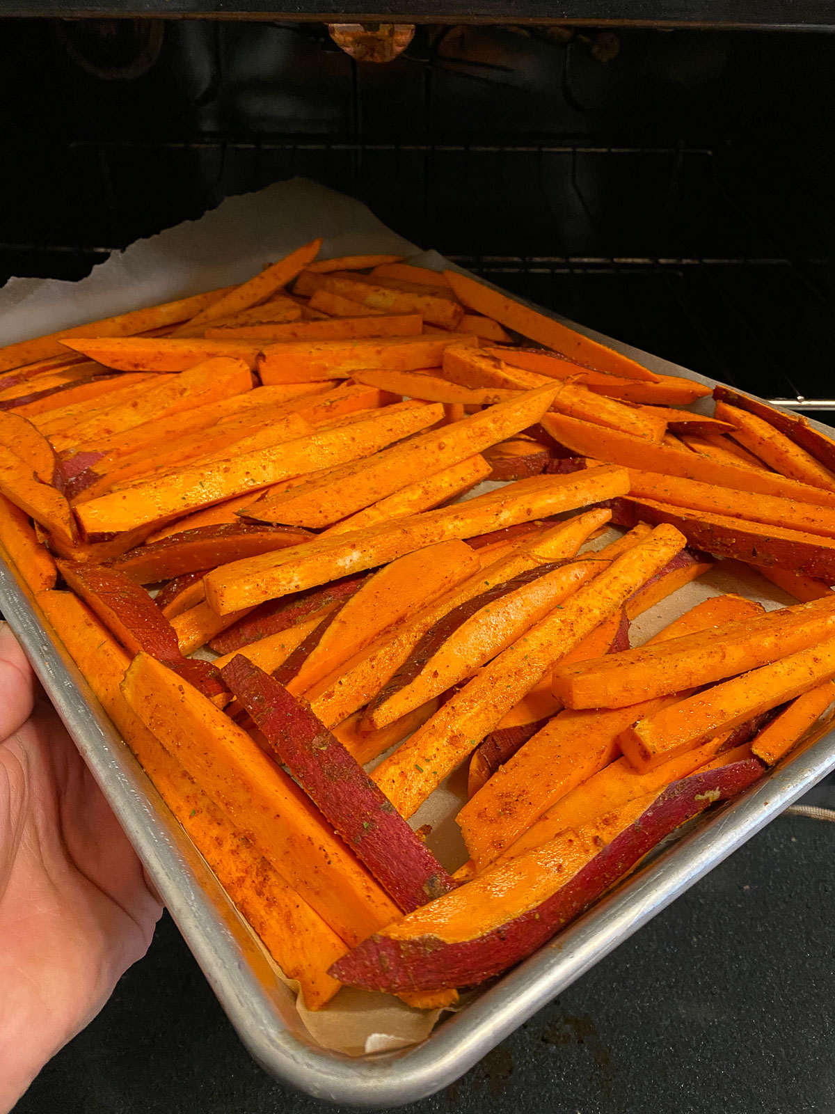 seasoned sweet potato fries in a baking tray being placed in the oven