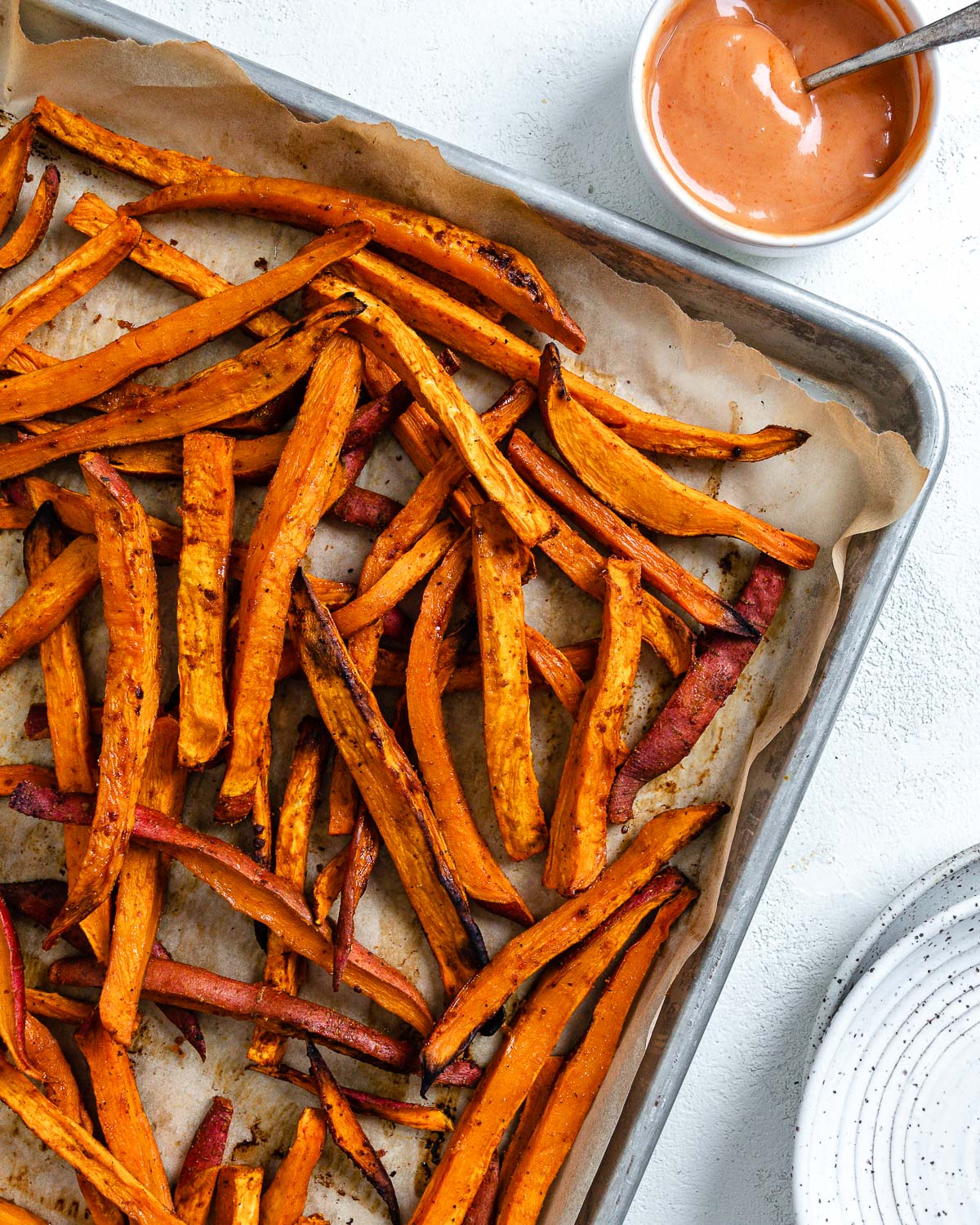 completed sweet potato fries in a baking tray with a small bowl of sauce