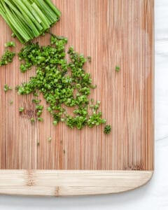 cut up chives on a brown cutting board