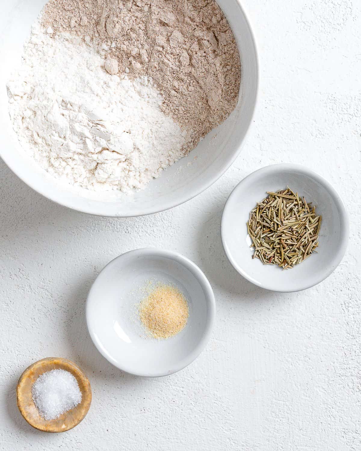 ingredients for Rosemary Vegan Crackers measured out in small white bowls against a white surface