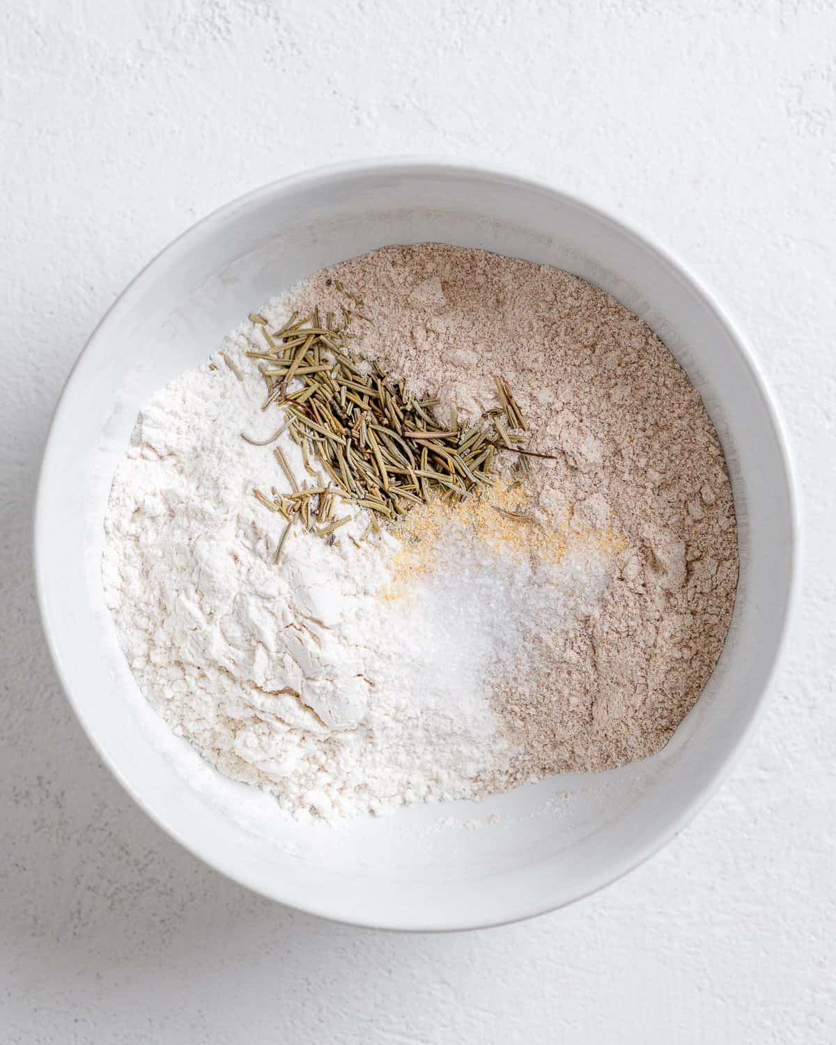 process of the addition of flour and spices in a white bowl against a white background