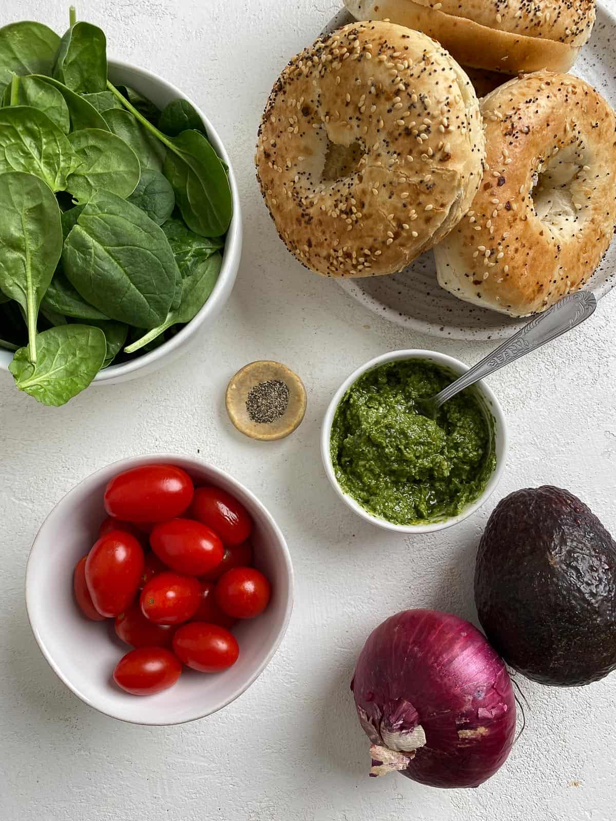 ingredients for Vegan Bagel Sandwich with Pesto measured out against a white surface