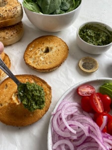 process shot of adding pesto to a bagel with ingredients on the side