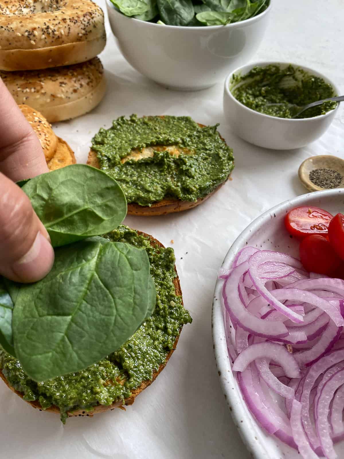 process of adding spinach on top of pesto with ingredients on the side