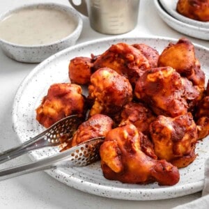 completed BBQ Cauliflower Wings plated on a white plate with a bowl of sauce in the background