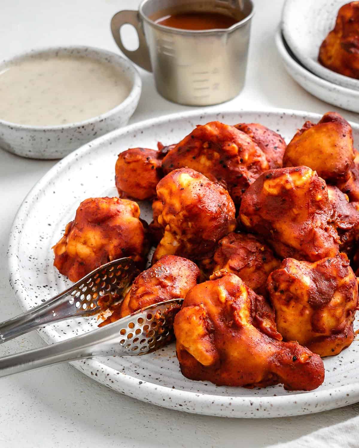 completed BBQ Cauliflower Wings plated on a white plate with a bowl of sauce in the background