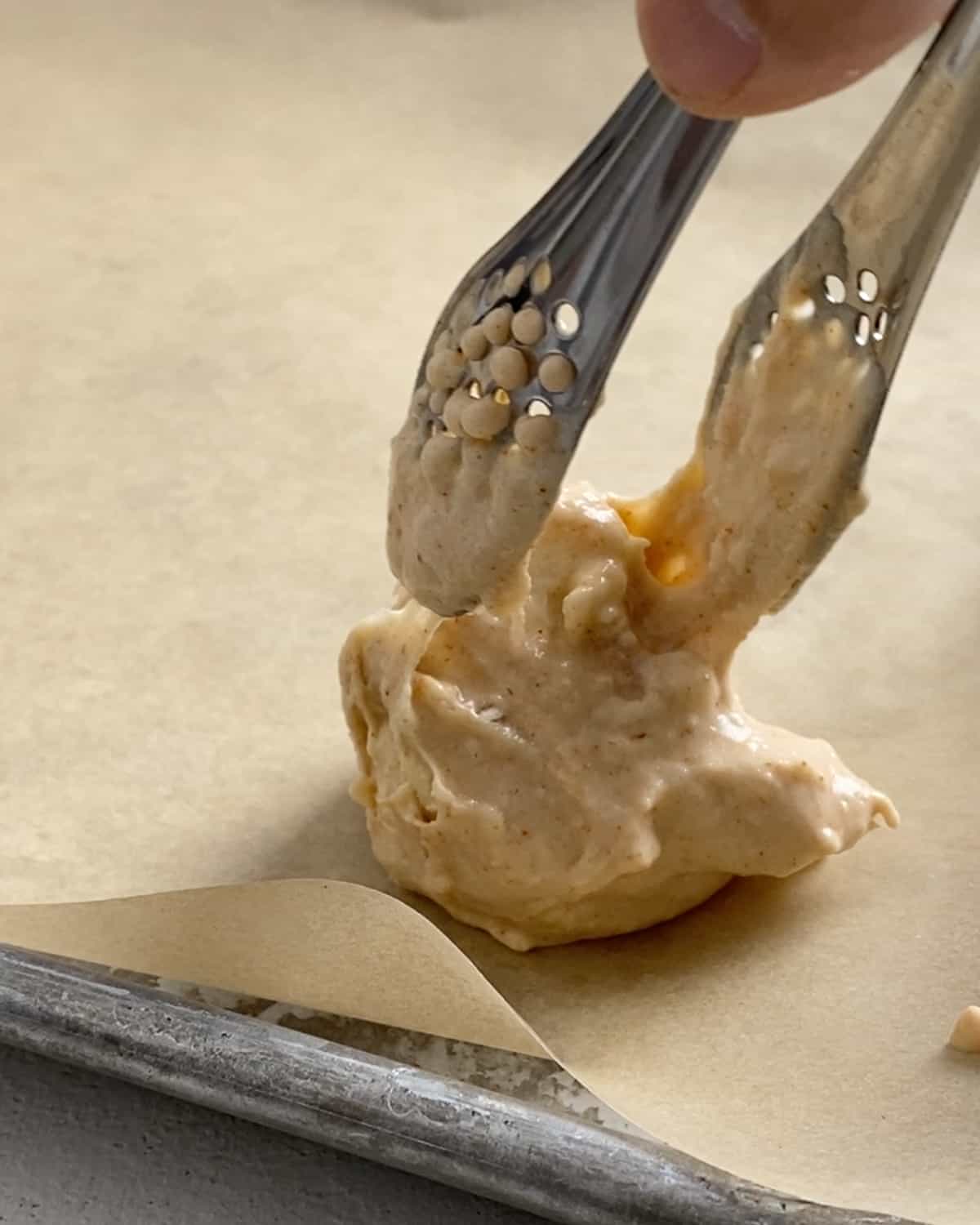 process shot of placing a cauliflower floret with batter on parchment paper with tongs