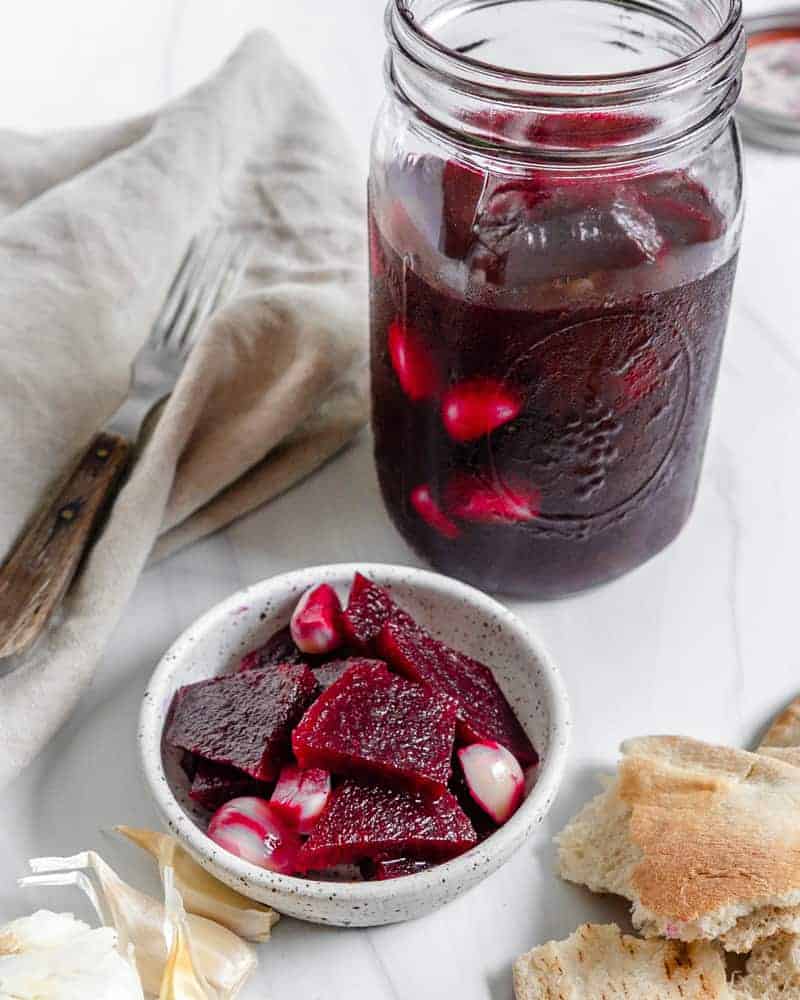 completed Small Batch Pickled Beets in a small bowl and mason jar against a white. background with several ingredients in the background