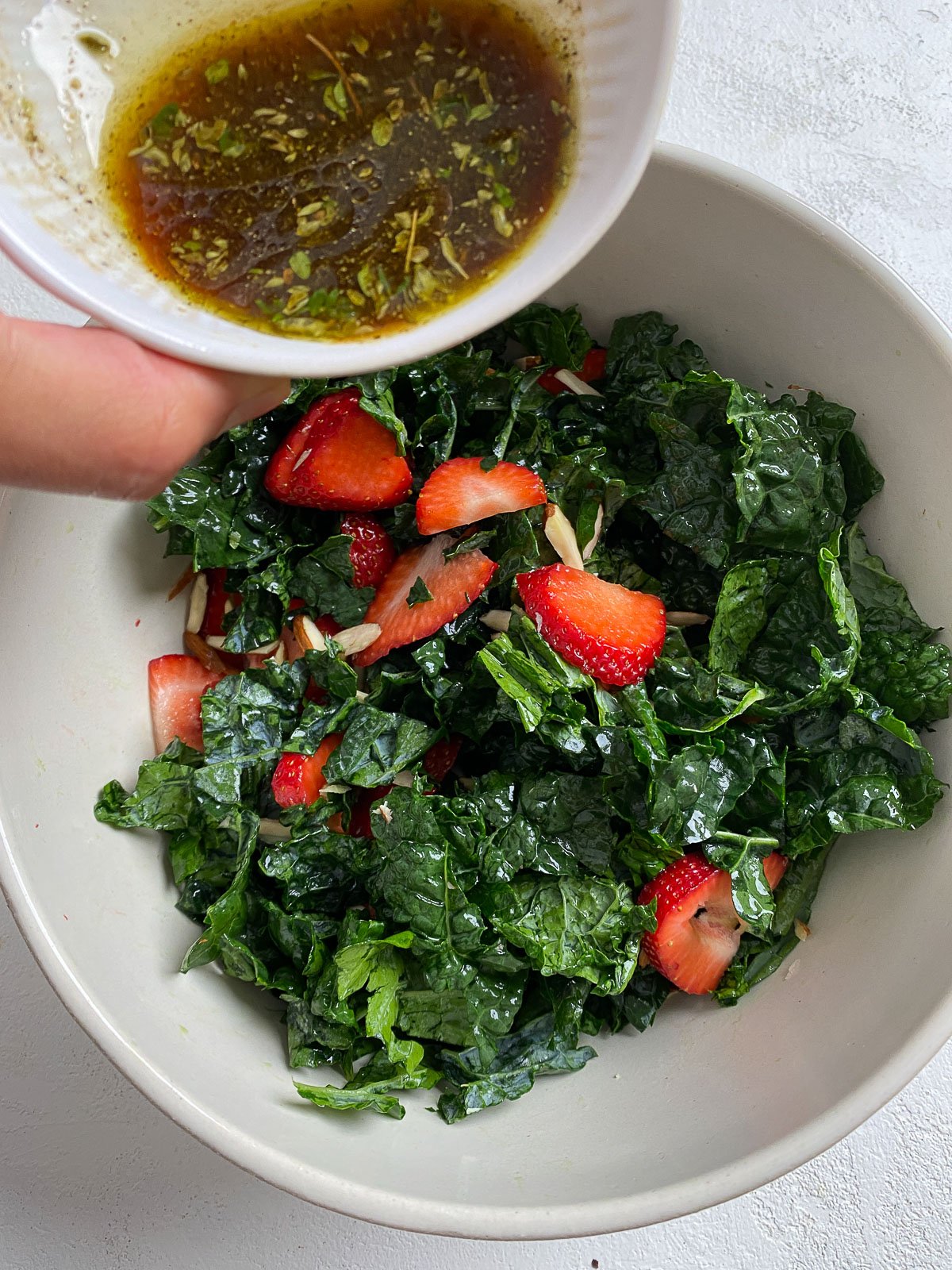 process showing addition of dressing into bowl of strawberry kale salad