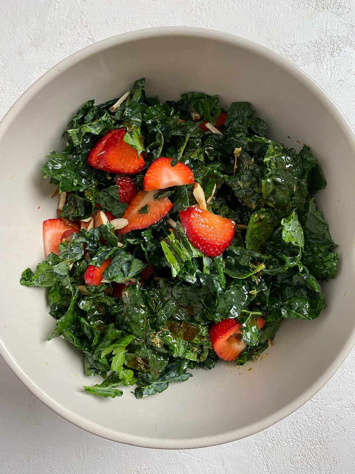 process showing post mixing of dressing into bowl of strawberry kale salad in white bowl