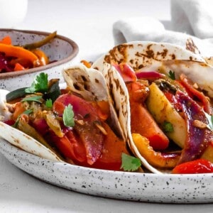 completed Grilled Veggie Fajitas on a white speckled plate with veggies in the background