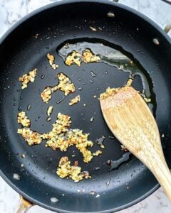 process of garlic and oil being sautéed in a black pan