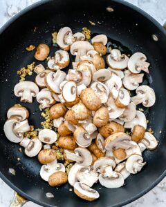 process of mushrooms being sauteed in a blak pan