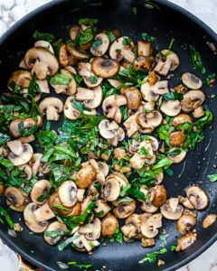 process of mushrooms and greens being cooked in a black pan