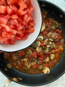 process of adding tomatoes to black pan of spicy tomato basil pasta dish
