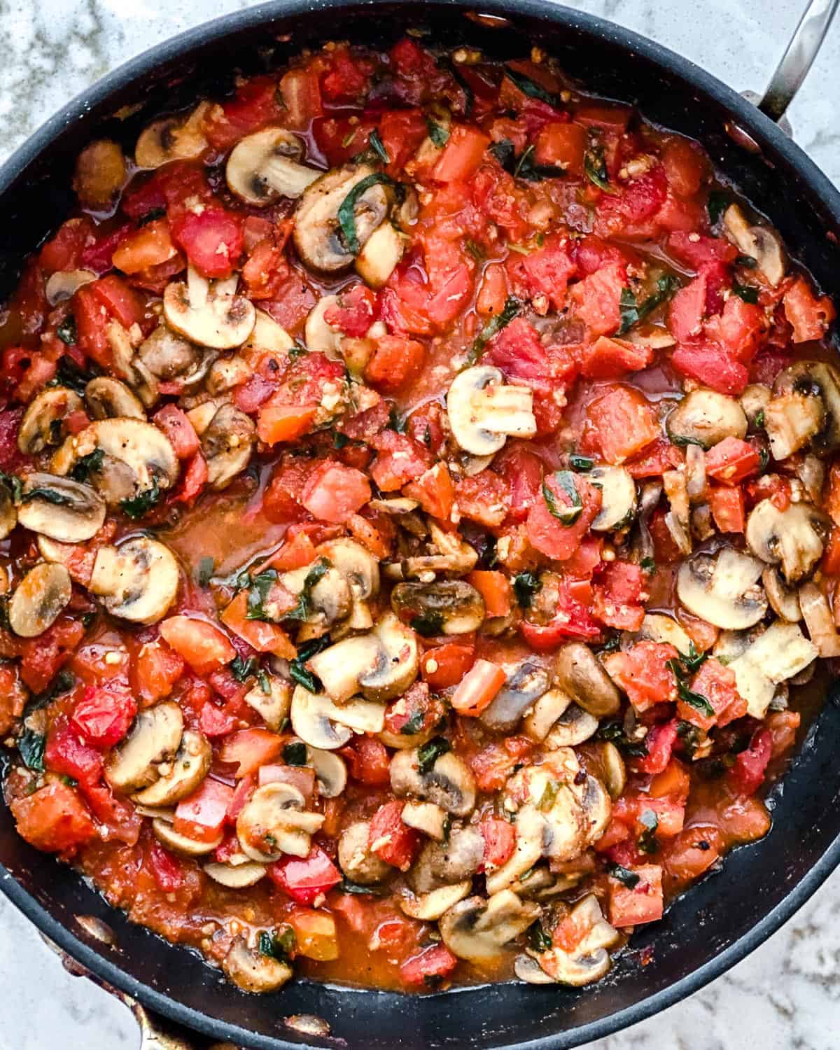 process of cooking completed Spicy Tomato Basil Pasta in a white plate against a white surface in a black pan