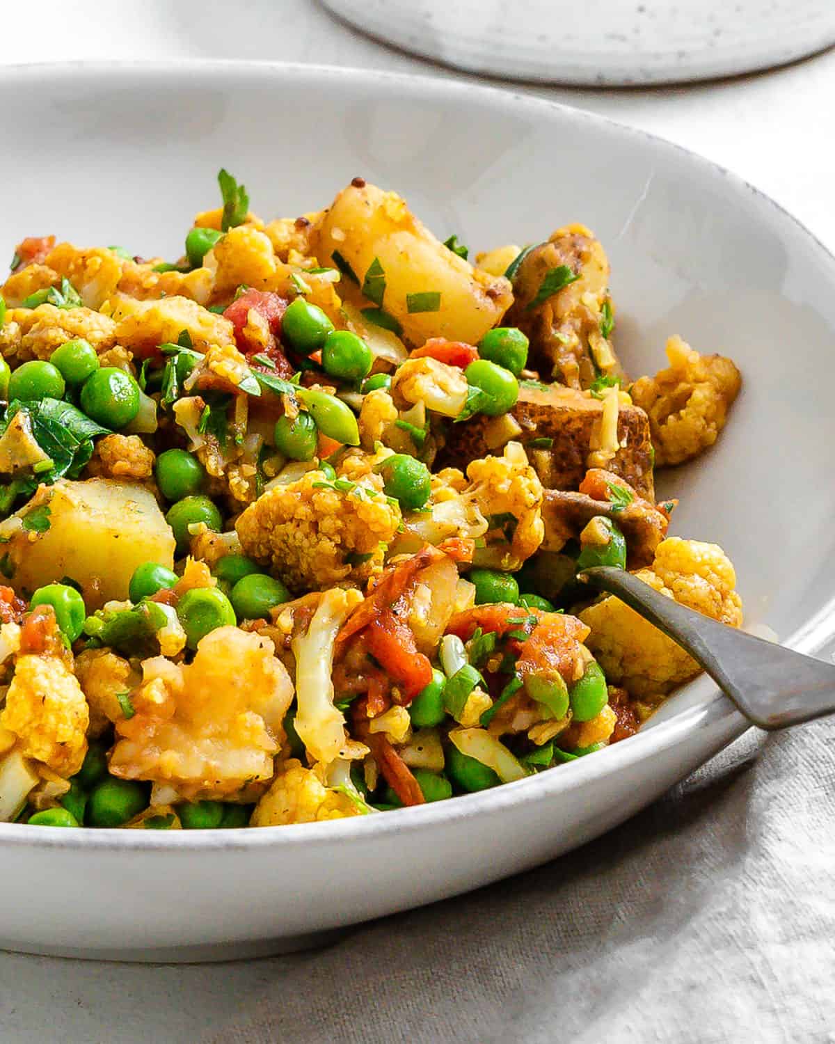 complete Aloo Gobi (Curried Potatoes, Cauliflower, and Peas) in a white bowl