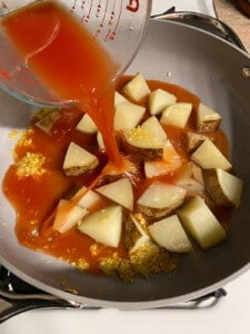 process of adding tomatoes to pan of potatoes
