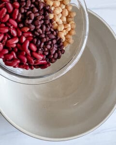 process of adding mixed bean salad ingredients into a white bowl