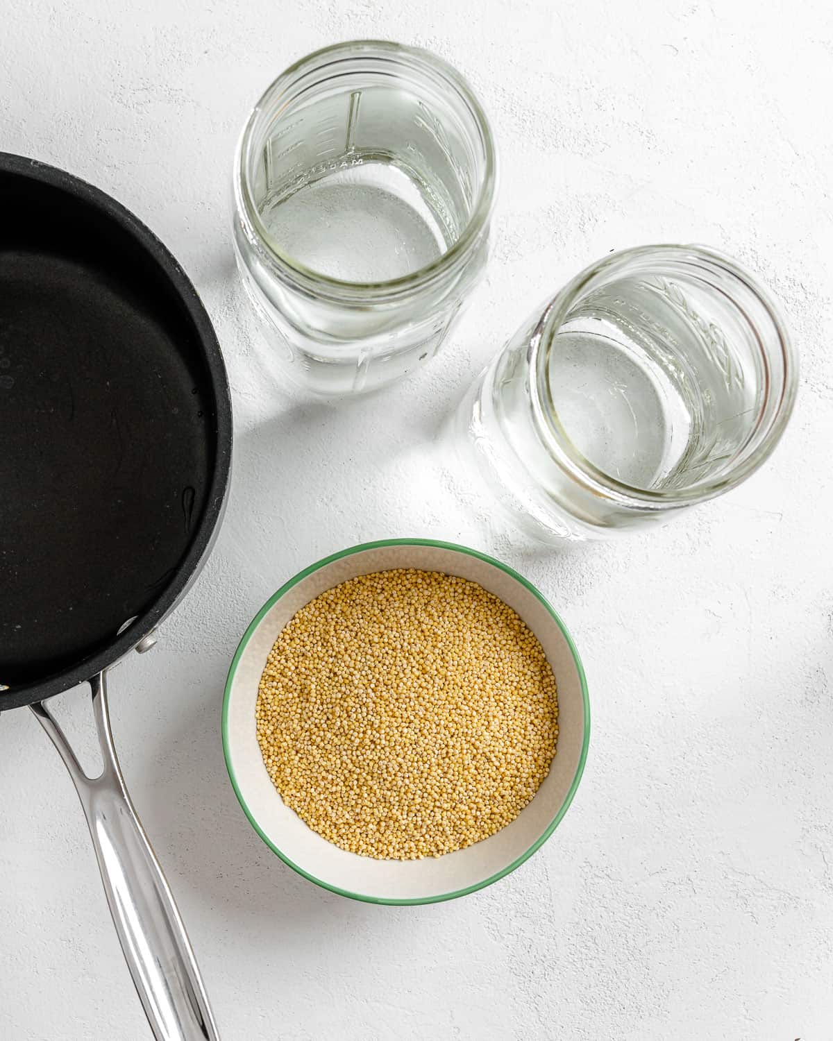 one black pan, two jars and a bowl of millet against a white background