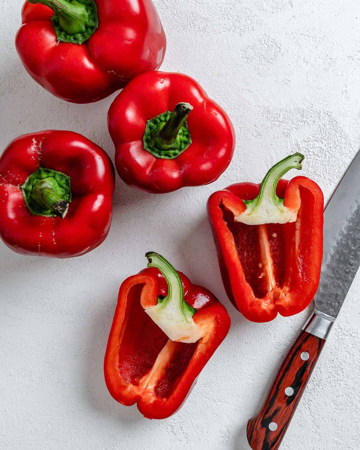 three red bell peppers and one red bell pepper halved on a white surface
