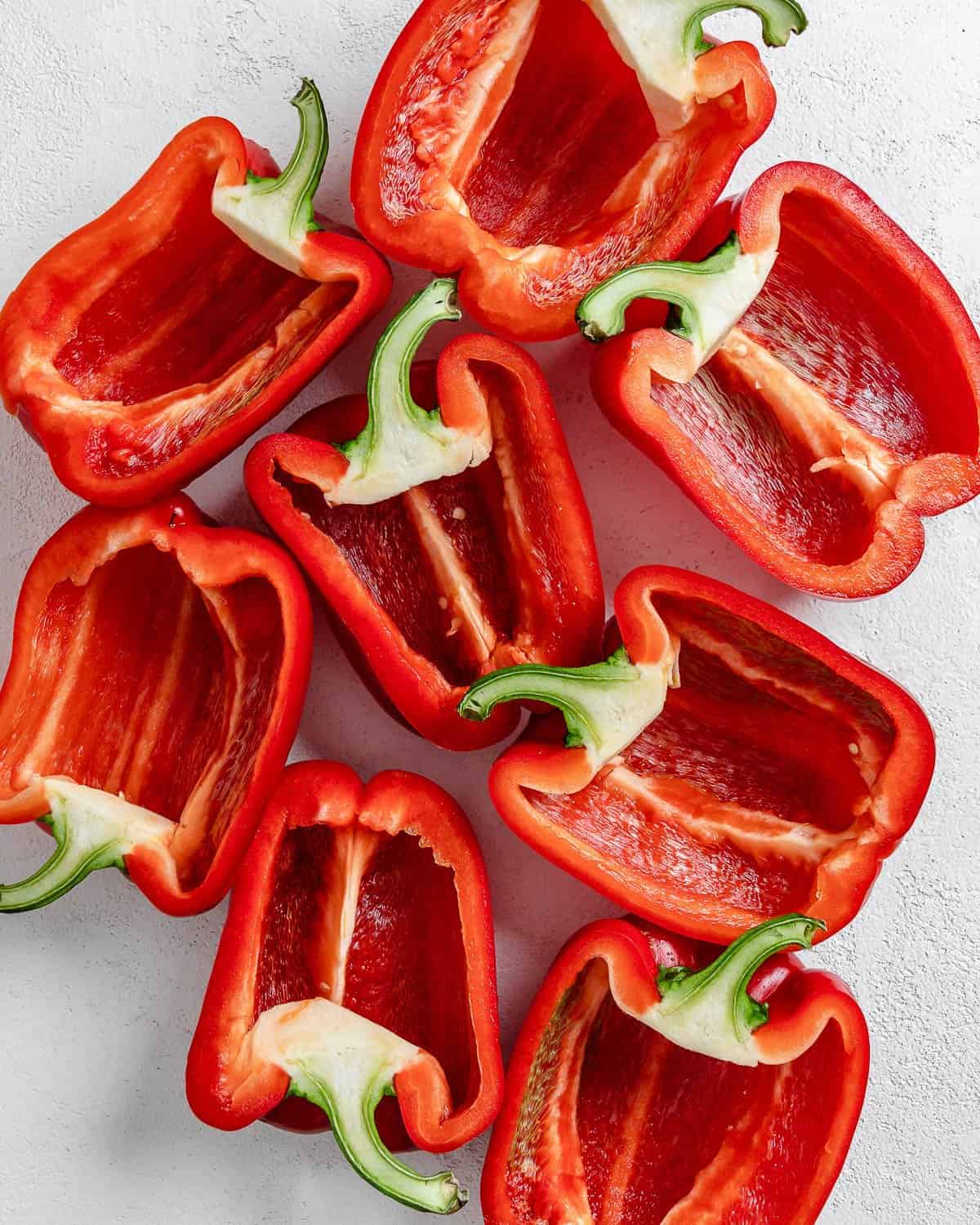 8 halved red peppers on a white surface