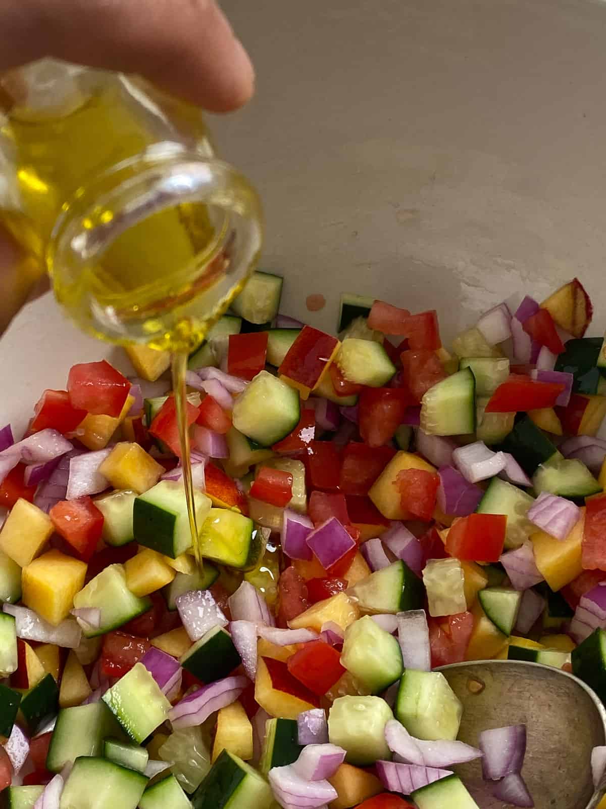 olive oil being added to bowl of veggies