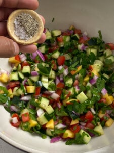 salt and pepper being added to bowl of veggies