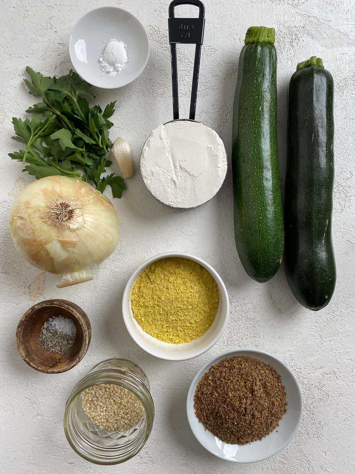 ingredients for Vegan Baked Zucchini Fritters measured out and separated on a white surface