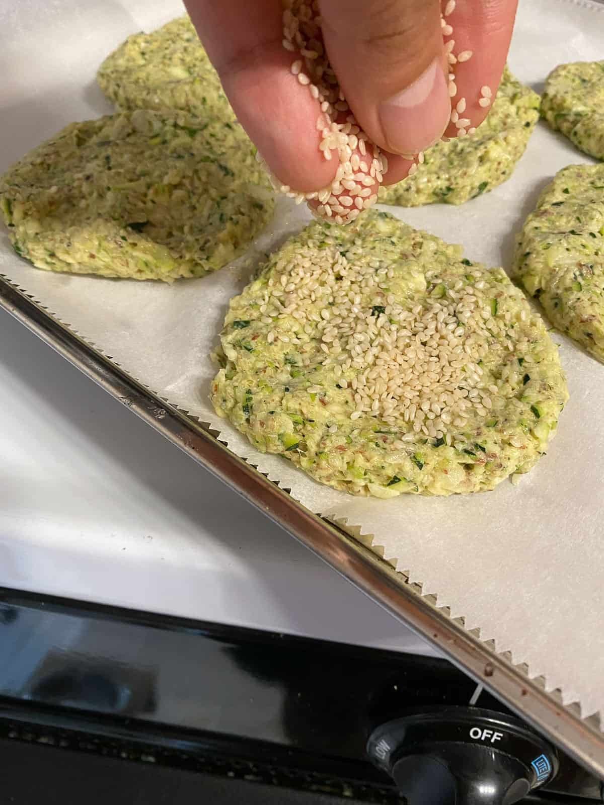 process shot of adding sesame seeds to circular shaped zucchini fritters